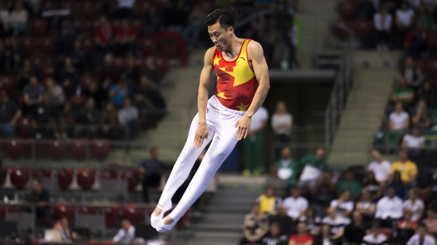 Photographie couleur du chinois Dong Dong, champion olympique de Trampoline, en train d'effectuer un salto en position tendu