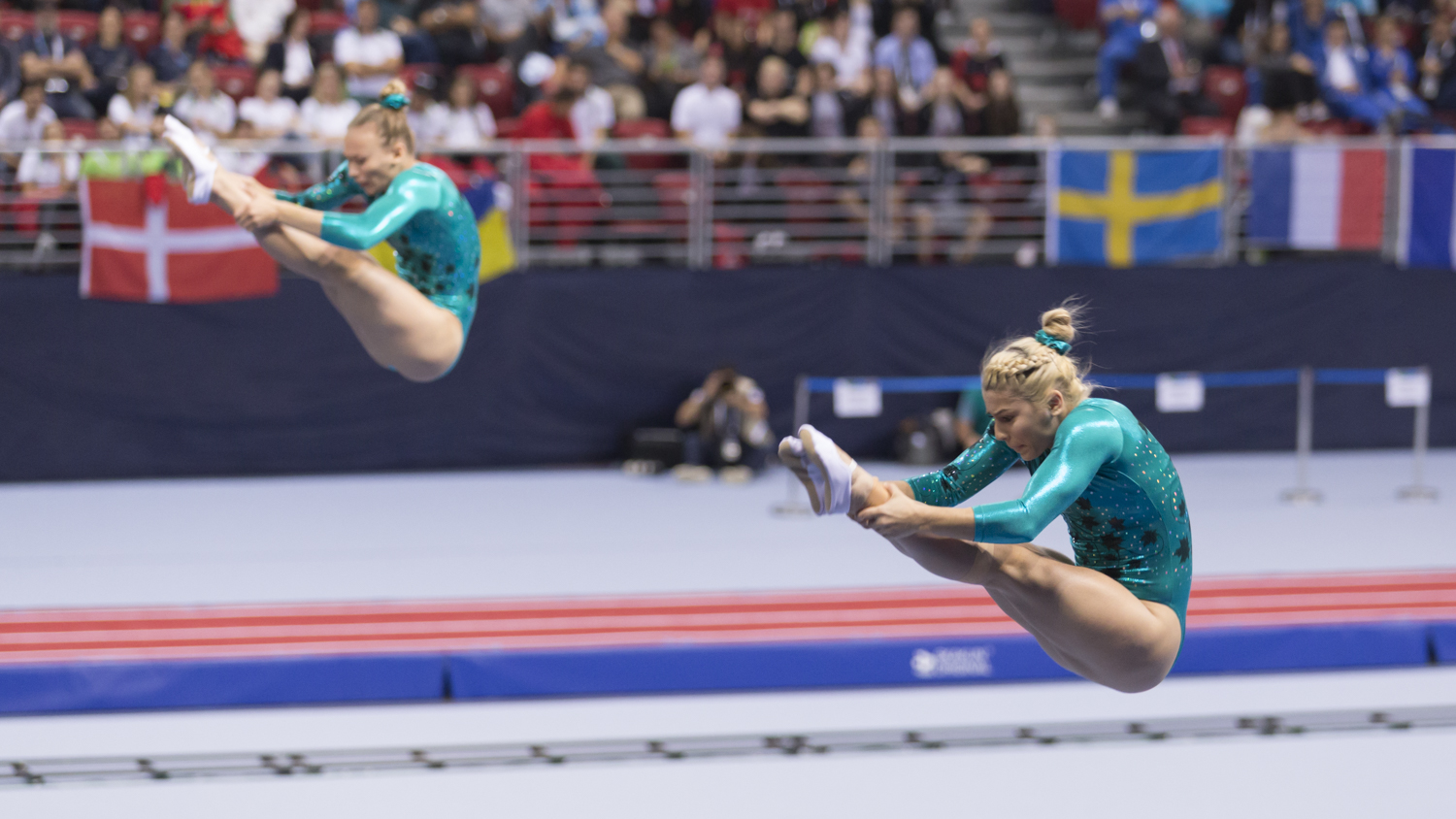 Photographie couleur de deux gymnastes femmes qui concourent en Trampoline synchronisé et se trouvant en position de salto avant carpé