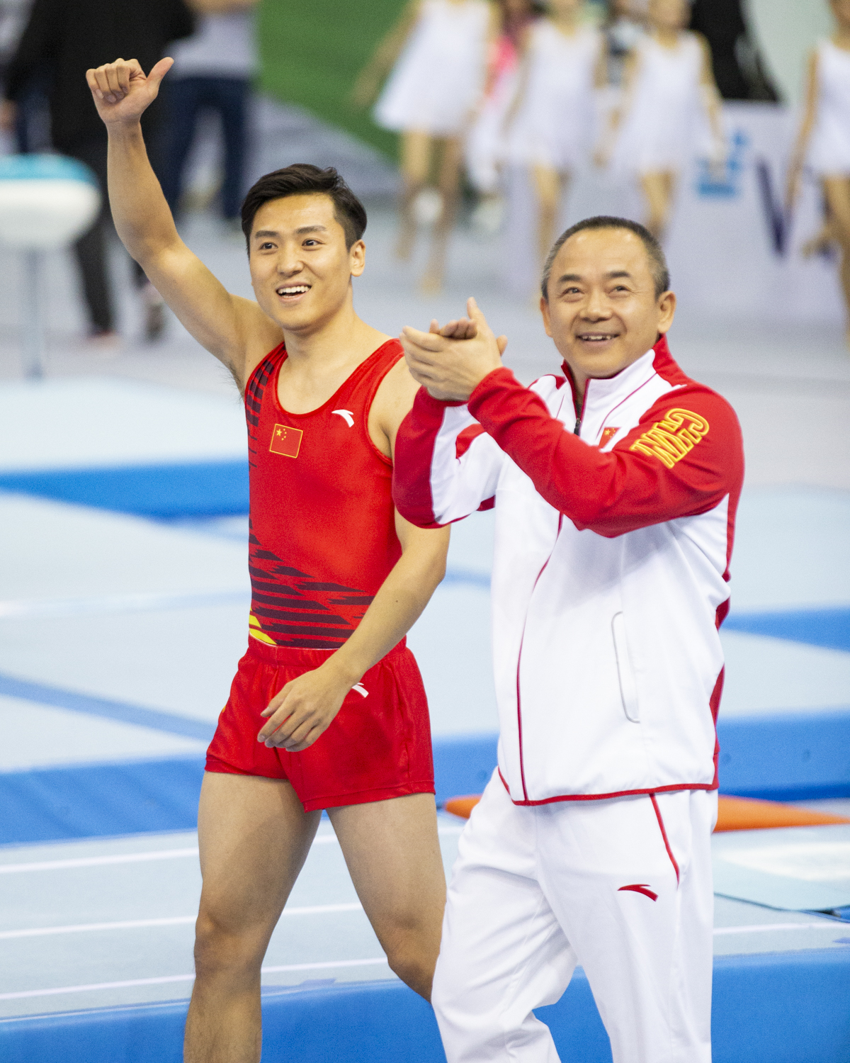 Photographie couleur du chinois Dong Dong, champion olympique de Trampoline, et de son entraineur qui semblent heureux face au public