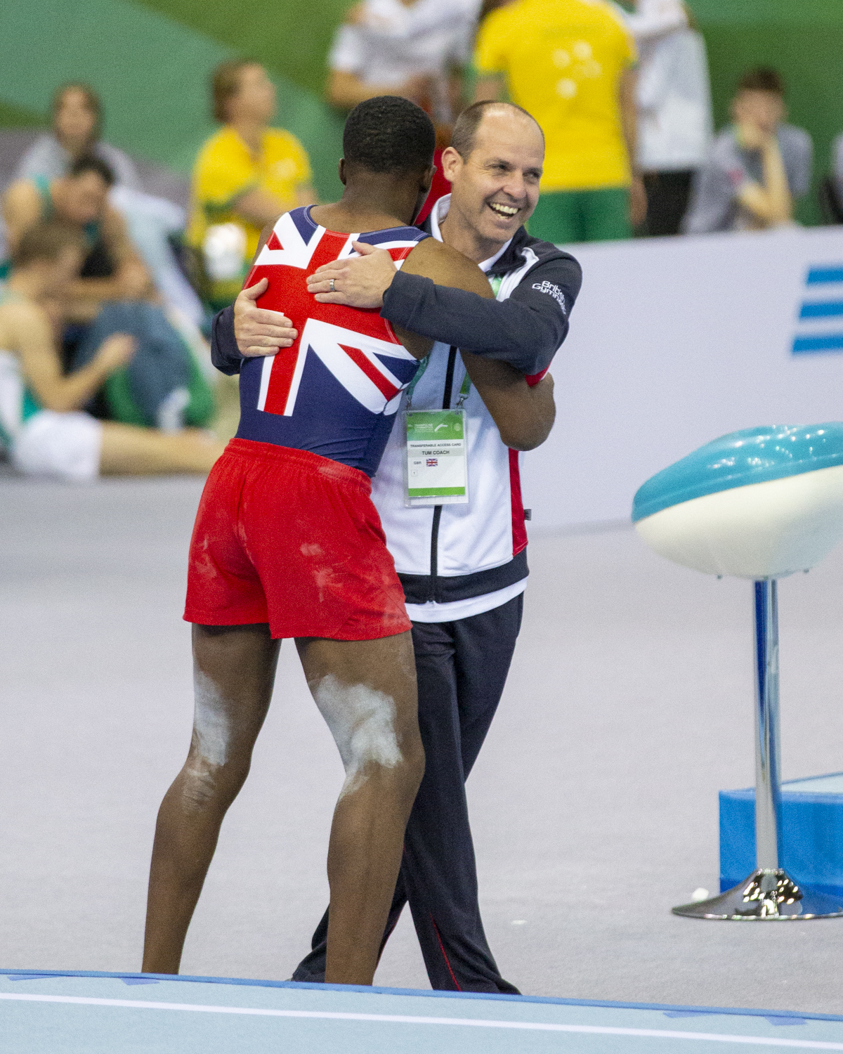 Photographie couleur du britannique Dominic Mensah, champion du monde de Tumbling par équipe, et de son entraineur s'enlaçant avec un visage heureux après le passage en Tumbling