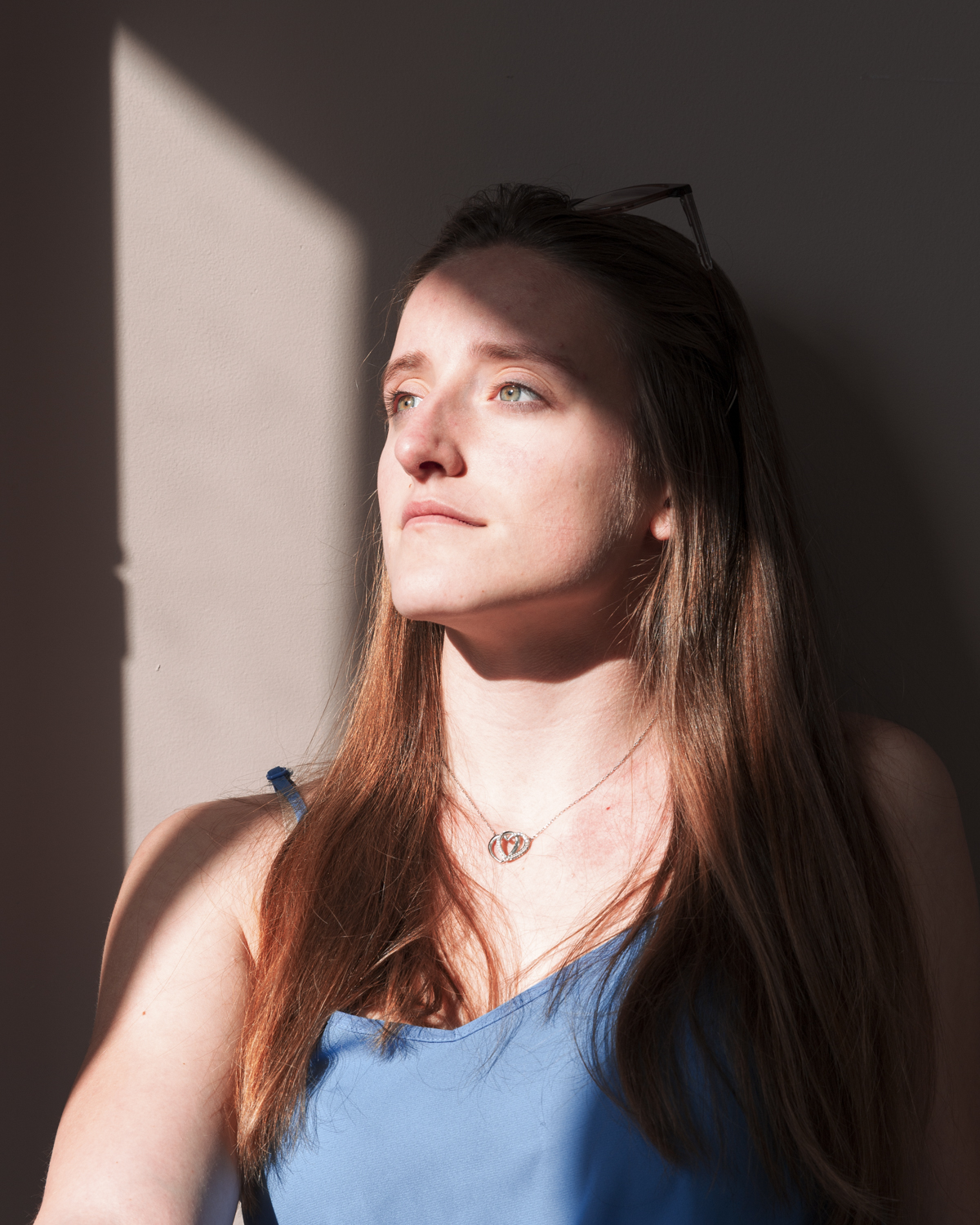 Photographie couleur de Cécile Reiter qui dirige son regard vers l'extérieur ensoleillé pendant le confinement
